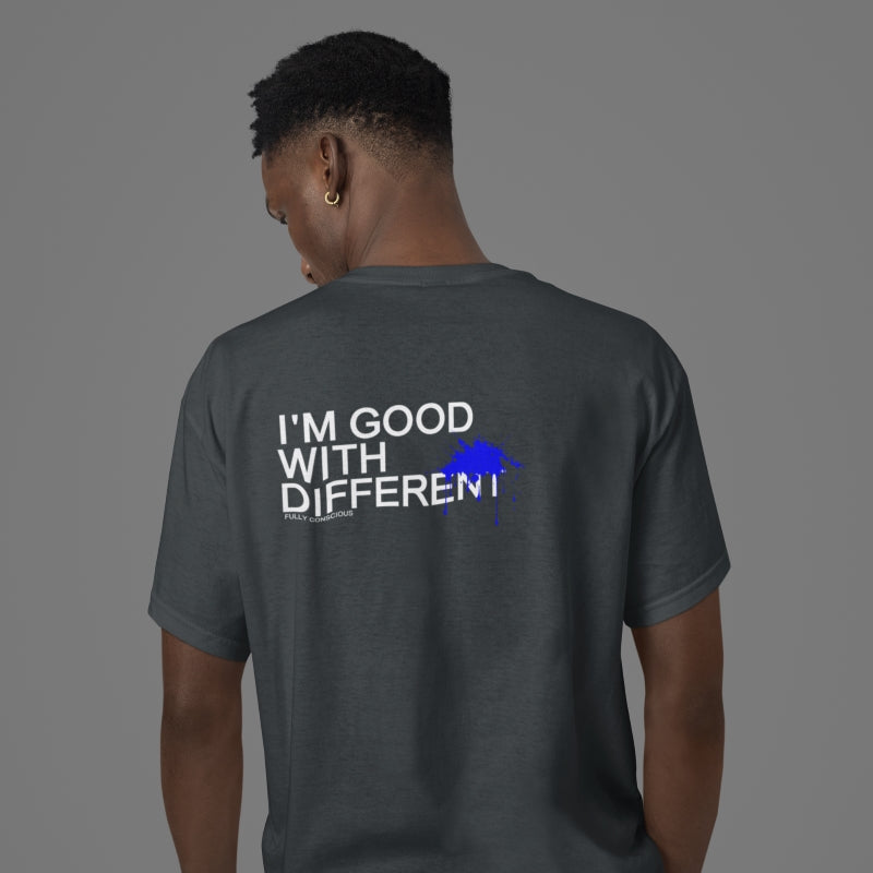 Man wearing a grey “I’M GOOD WITH DIFFERENT™” inspirational T-shirt from Fully Conscious Apparel, standing indoors against a neutral backdrop; modern motivational apparel promoting individuality and confidence.