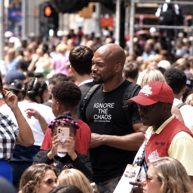 Man in a black IGNORE THE CHAOS t-shirt by Fully Conscious Apparel standing in a crowded Times Square